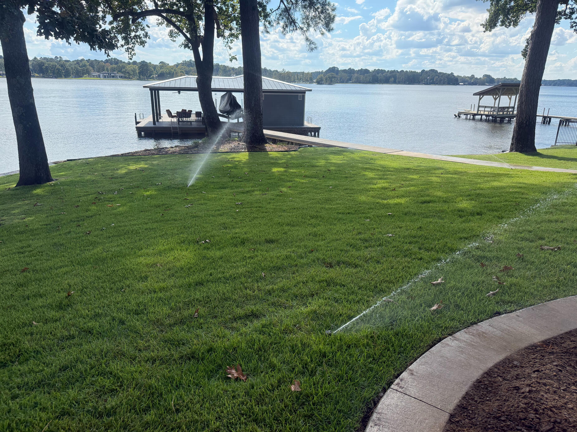Dual sprinkler heads watering a lakefront lawn at Lake Cherokee near Longview, Texas. Custom irrigation systems designed for efficient lake property watering in East Texas.